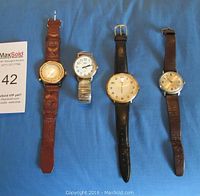 Four Timex wristwatches laid side by side on blue fabric background, showing overall condition and bands.