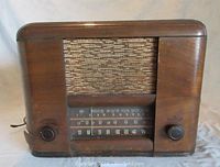 Front view of vintage wooden radio with woven speaker grille, dial, and two knobs.