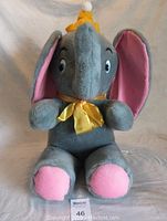 Front view of the 22-inch plush Dumbo showing gray body, pink inner ears and feet, yellow party hat and bow.