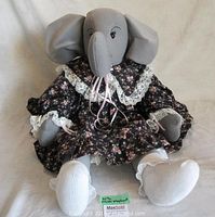 Front view of the handcrafted elephant plush toy sitting, showcasing the floral dress with lace and pantaloons.