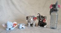 Four Ty Beanie Baby elephant plush toys of different sizes and colors arranged in a row.