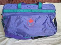 Full view of purple duffle bag with green accents and red Canadian Olympic logo embroidered on front pocket.