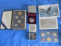 Full view of the four coin sets and single coins on a blue background with their respective folders, boxes, certificates, and cards.
