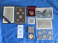 Photo showing the three coin sets: an Uncirculated Set in original package with six coins, a Specimen Set in original sleeve with six coins, a Proof Silver Dollar in a red display case, and a Brilliant Uncirculated Silver Dollar coin in plastic sleeve with certificates and informational cards.