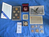 All four coin sets displayed on blue cloth including specimen set in plastic, uncirculated set in blue packaging, proof silver dollar in red box, and brilliant uncirculated silver dollar with certificates.