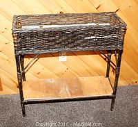 Front view of wicker planter with tin liner inside, showing the plywood shelf below and the planter's condition.