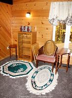 Overall view of upholstery chair with cane sides, wood TV tables, rugs, mirror, and stereo stand.
