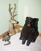 Photo showing the full lot including the brass deer sculpture, solid wood bear carving, and small cast figure on carpeted floor against wall with electrical outlet visible.
