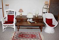 Photo showing two white wicker chairs with red cushions, wood coffee table and matching end tables, three table lamps, and patterned rug.