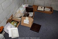 Wide shot of multiple boxes containing various collector plates, certificates, and porcelain dishes placed on floor showing packaging and certificates.