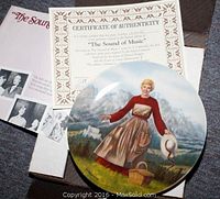 Close up of Knowles 'The Sound of Music' plate featuring a woman in a dress holding a hat by a basket with accompanying certificate of authenticity and box.