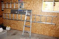 Three aluminum ladders, including a 5 ft step ladder, a 24 ft extension ladder mounted on wall, and an articulating ladder in packaging.
