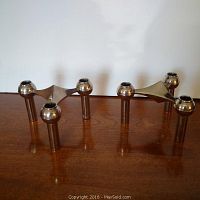 Pair of silver color metal Scandinavian style candelabras displayed on wooden surface against white background. Both have three candle holders connected with a triangular central part.