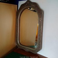 Front view of the antique decorative frame showing oval mirror and detailed silver metalwork on the frame edges and top floral motif.