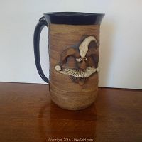 Full side view of large stoneware mug showing brown textured surface and navy blue handle and rim, with sculpted jester face on front.