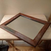 Full view of antique solid oak framed mirror lying on a wooden table, showing the aged solid wood frame and mirror glass surface.