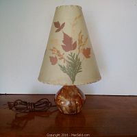 Front view of ceramic lamp base with mottled brown glaze and floral cream fabric lampshade decorated with orange, red, and green leaves
