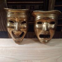 Front-facing view of the brass comedy and tragedy theatre masks side by side on a wooden surface.