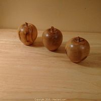Three life-sized hand-turned burl wood apples arranged in a row on a wooden surface showing their shape, size, and wood grain variations.
