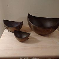 Set of three crescent-shaped brass alms pots on wooden surface, showing size differences and patina