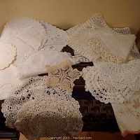 Overview of antique lace items spread out showing various doilies, handkerchiefs and napkins in white and beige lacework.