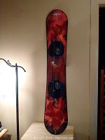Front view of 130cm freestyle snowboard showing top surface with flame-like artwork and two black bindings with blue padding.