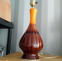 Front view of mid century modern ceramic table lamp showing orange to brown glossy glaze, bulb socket, and cord on wooden surface.