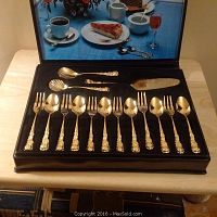 Full set of 15 gold plated dessert pieces displayed in a fitted black molded tray inside a faux snakeskin gift box. Includes spoons and forks with decorative floral handles.