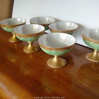 Set of six sherbet cups arranged in two rows on a wooden surface, showing gold and green painted decoration and interior lustre glaze.