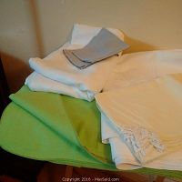 Stack of folded linens including green tablecloth, white and yellow lace-edged napkins, and gray napkins.