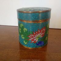 Side angle view of the cylindrical cloisonné box showing turquoise enamel with colorful floral patterns and brass rim.