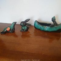 Photo of three pottery items: ceramic canoe planter with figure, seal figurine, and bunny figurine on wooden surface.