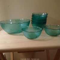 Overall view of one large bowl and ten smaller bowls in turquoise glass with crackled texture and leaf design.