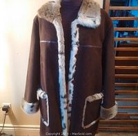 Front view of dark chocolate brown winter jacket showing spotted light faux fur trim on collar, front edges, pockets, and cuffs. Jacket displayed on mannequin with purple shirt underneath.