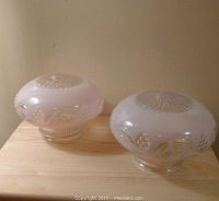 Pair of pink glass light shades side by side on wooden surface