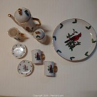 Overhead shot showing full miniature Christmas coffee set including coffee pot, creamer, sugar bowl, two cups, two saucers, and a plate with cardinal and holly decorations.