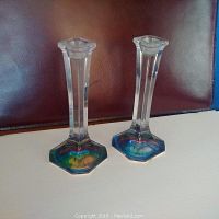 Two clear lead crystal candle sticks with hexagonal bases showing rainbow effect, standing on a white surface against a brown background.