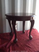 Full side view of the round rosewood end table placed on red cloth, showing round top, high gloss finish, and curved legs with ball feet.