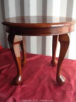 Full side view showing the round table top and cabriole legs with rounded feet on a red cloth background.