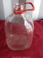 Front and side view of vintage glass gallon milk bottle with red handle showing overall condition and handle detail.