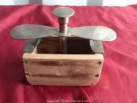 Top view showing wooden butter mold box with metal screw press and wing-shaped handle with wear and patina.