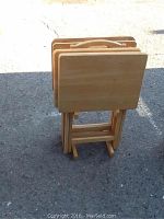 Set of four hardwood TV trays/tables folded and stacked upright, showing carrying handles and rectangular tabletops with rounded corners.
