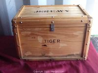 Front view of a wooden chest showing 'TIGER' stenciling and metal latch on the lid, along with metal rivet accents on edges.