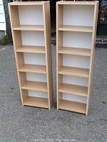 Front view of two light wood finish pressboard bookcases with four shelves each.