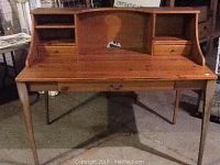 Front view of large pine desk with three drawers, shelving compartments on top, showing original wood surface and replaced legs.