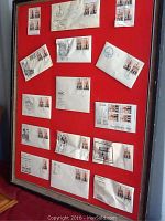 Framed display showing overall arrangement of 14 envelopes with stamps on red backing, black frame visible, display worn but stamps intact