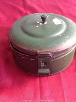 Closed green metal container with lid and latch, showing signs of wear and paint chipping.