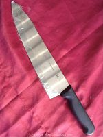 Full view of the 10-inch chef's knife showing the blade and black handle on a red surface.