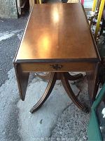 Full view of the table with one drop leaf extended and the other dropped down, showing table shape and base.