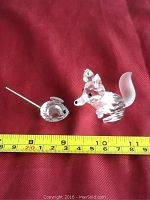 Both Swarovski crystal animal figurines placed on a red fabric with measuring tape to show size approximately 2-3 inches.